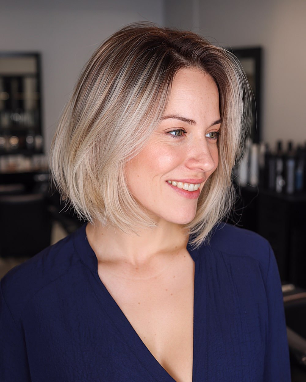 Champagne blonde balayage on a short graduated bob with dark brown roots and side part
